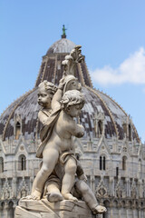 A detailed close-up of a cherub statue is positioned in the foreground, with the iconic dome of the Pisa Baptistery visible and in soft focus behind it. Perfect for travel blogs, historical art conten