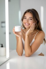 Woman around 30 sitting by bathroom mirror, holding jar of cream and smiling, bright minimalist interior
