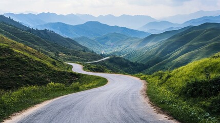 Fototapeta premium Winding road through lush green mountain valleys. Misty peaks in the distance