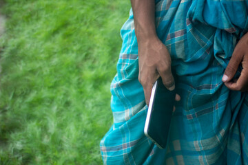 Man holding a smartphone in his hand, wearing a blue lungi