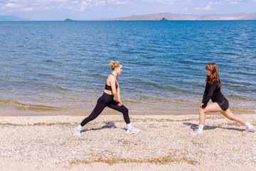 Two women exercise on a beach while enjoying the sunny day by the water