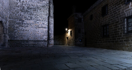 A dark alleyway of a medieval town with a street lamp shining on a brick wall