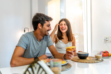 Happy couple enjoying breakfast and laughing together at home