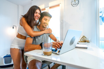 Happy couple working from home using laptop in bright modern apartment