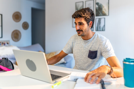 Focused young man working from home using laptop and reading notes