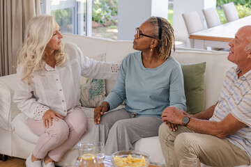 Senior friends sitting on sofa, enjoying conversation and snacks at home