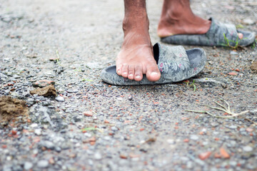 Close up of a persons bare foot wearing a worn sandal on a gravel path