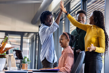 Team celebrating success in modern office, high-fiving with joyful expressions