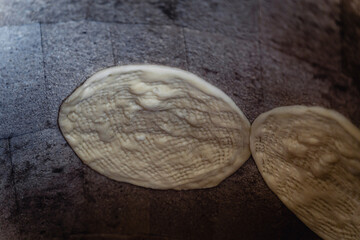 Uzbek flatbreads are baked in tandoor. They hang on wall of tandoor and begin to brown.