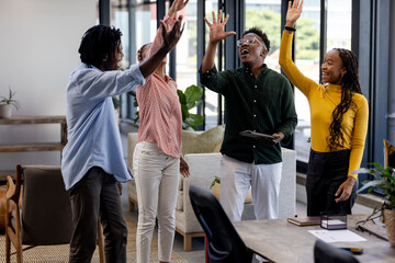 Diverse team celebrating success with high fives in modern office space