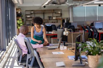 Collaborating at office desk, colleagues discussing project with documents and laptop