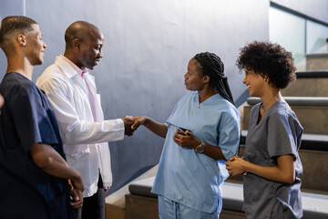 In hospital hallway, medical professionals in scrubs shaking hands with colleague