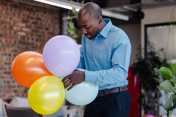 Businessman in blue shirt arranging colorful balloons at office celebration event