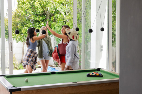 Women celebrating with high fives near pool table, enjoying leisure time together