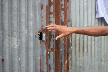 A hand reaches towards a hole in a rusty corrugated metal wall