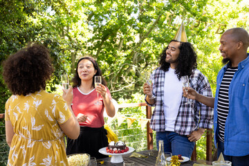 Friends celebrating outdoors with champagne, wearing party hats, enjoying sunny day