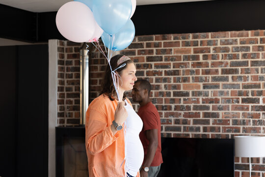 Celebrating at home, pregnant woman holding balloons with family around her