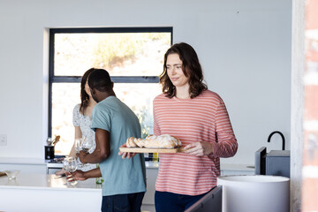 Friends preparing meal together in kitchen, carrying bread and setting table