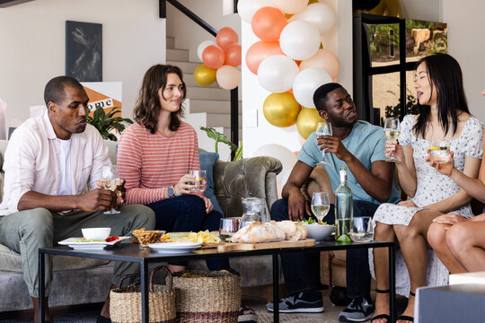 Celebrating at home, friends sharing drinks and snacks, laughing and talking