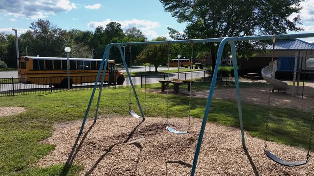 Empty chute on playground of school with yellow school bus on parking lot. Sunny summer day in city. Aerial rising shot.
