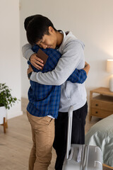 Two people hugging warmly at home, one holding passport and suitcase