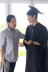 Proud father congratulating son in graduation gown, sharing joyful moment at home