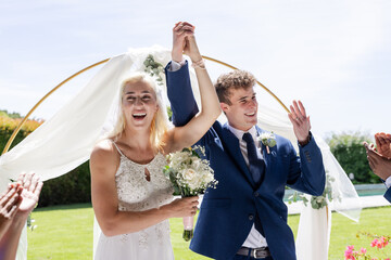 Bride and groom celebrating outdoors, holding hands and smiling joyfully