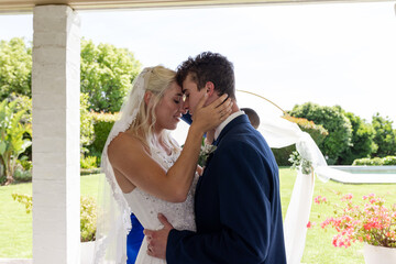 Embracing lovingly, bride and groom in outdoor wedding ceremony surrounded by nature