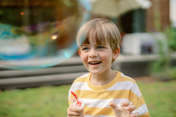 A young boy smiles joyfully while blowing bubbles in a sunny backyard. The bright atmosphere captures the essence of childhood fun and exploration in nature.