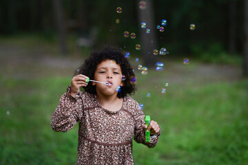 Girl blowing colorful bubbles in grassy outdoor area.