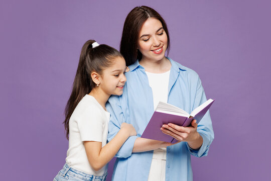 Young woman wear blue casual clothes have fun with child baby girl 8-9 years old Mommy little kid daughter read book fairytale before sleeping isolated on plain purple background Mother's Day concept