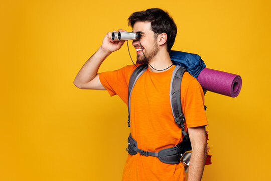 Young traveler man carry backpack with stuff mat hold use binocular isolated on plain yellow background. Tourist leads active healthy lifestyle walk on spare time Hiking trek rest travel trip concept