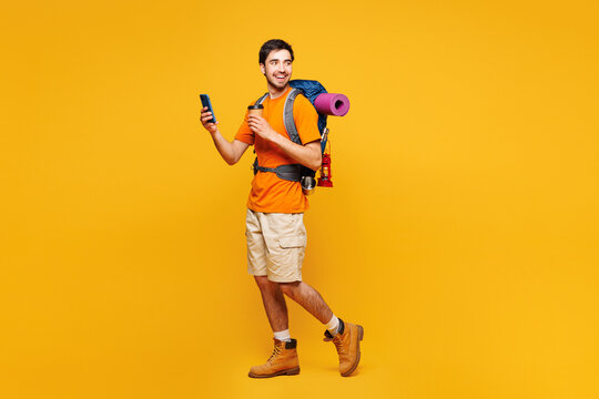Young traveler man carrying backpack with stuff mat mobile cell phone coffee isolated on plain yellow background Tourist lead active lifestyle walk on spare time. Hiking trek rest travel trip concept