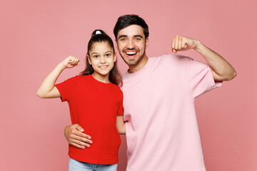 Young fun parent man with child girl wear red casual clothes. Daddy little kid daughter show biceps muscles on hand, strength power isolated on plain pink background. Father's Day Love family concept.