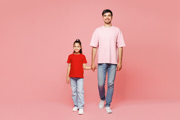 Full body young happy parent man with child girl wear red casual clothes. Daddy little kid daughter hold hands walk go look camera isolated on plain pink background. Father's Day Love family concept.