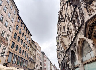 Obraz premium A view up at the various architectural styles of different eras of buildings in the historical part of Munich while walking along quiet, cozy streets on a cloudy rainy summer day.