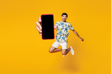 Full body young man he wearing blue beach t-shirt casual clothes jump high holding in hand use blank screen area mobile cell phone isolated on plain yellow orange background studio. Lifestyle concept.