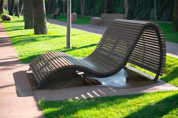 Wooden wave-shaped park lounger. Alley in the city public park with a recreation area