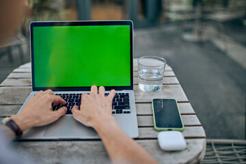 Hands Typing on Laptop Outdoors with Smartphone and Glass of Water Nearby