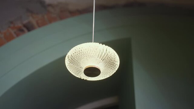 Modern pendant light with intricate glass texture glows warmly while suspended from ceiling inside stylish space featuring soft green tones and exposed brick accents adding charm to ambient setting
