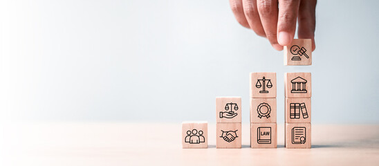 Business hand stacking wooden blocks with law and justice icons on light background. Concept of legal service, justice system, compliance, and business law consulting.