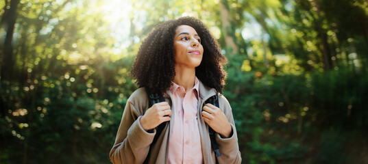 Woman, nature and trees in forest with sunshine, space and inner peace for adventure trip. Happy, person outdoor and sunlight in woods with zen, positive and hiking trail for summer break wellness.