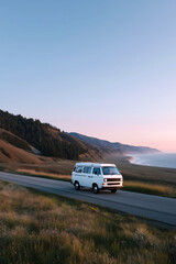 Obraz premium Vintage camper van road trip adventure on scenic coastal highway at sunset