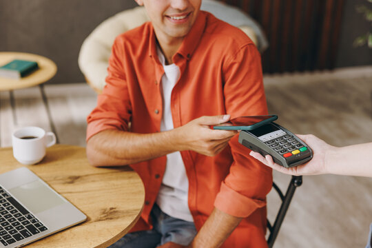Young happy man wear casual clothes hold bank payment terminal process acquire cell phone sit at table in coffee shop cafe relax rest in restaurant in free time indoor Freelance mobile office concept.