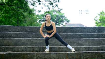 Fototapeta premium Female athlete wearing headphones, warming up before workout in urban park