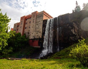Waterfall cascading down rocky cliff face beside modern building