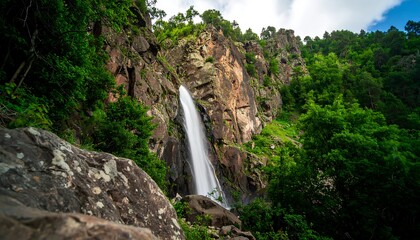 Waterfall cascading down rocky cliff face. Lush forest surrounds