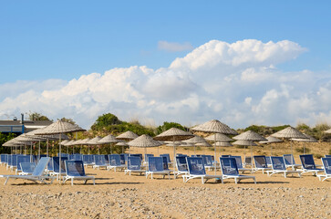 View of the sandy beach by the sea with sun loungers and umbrellas in the tourist area. Landscape with rows of sun loungers under umbrellas on the seashore.