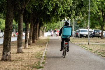 Fototapeta premium Delivery cyclist riding through tree-lined pathway