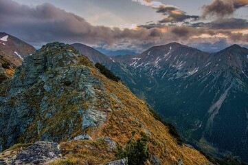Dramatic view of a rocky mountain ridge in the High Tatras during sunset. Scenic alpine trail with steep slopes, snow patches, and dramatic sky over rugged peaks in Slovakia.